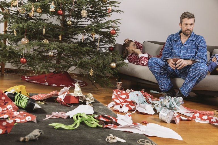 Tired couple in Christmas pyjamas looking at mess of wrapping paper