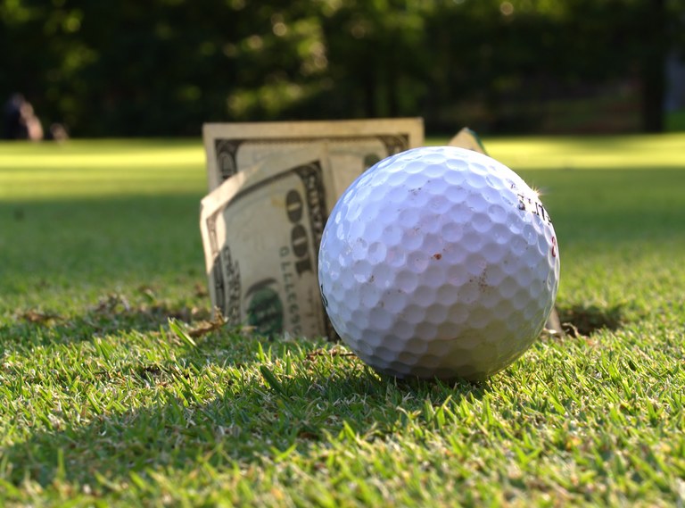 Closeup of golf ball by hole with $100 bills sticking out.