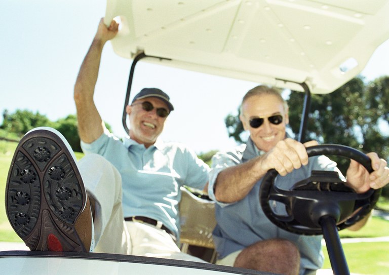 Two mature men in golf cart, smiling, close-up